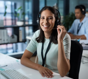 Young professional woman smiling while working in a modern office call center, representing financial independence for young professionals.