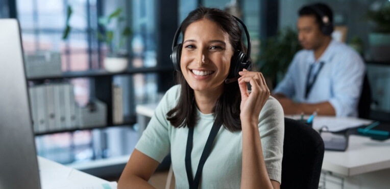 Young professional woman smiling while working in a modern office call center, representing financial independence for young professionals.