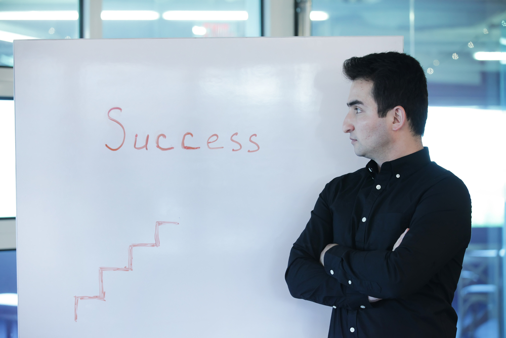 Horizontal indoors shot of call center leader standing at whiteboard with success word with arms crossed.
