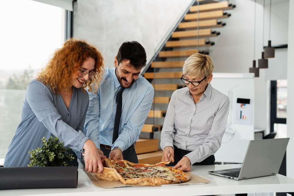 Office workers taking lunch break, pizza provided as a call center social perk so employees can eat together and relax.