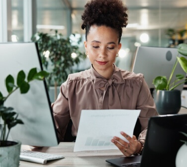 Business, woman and paperwork by computer in office for data entry in CRM system and reading revenue report. Account representative, employee and document for client sale stats and portfolio review.
