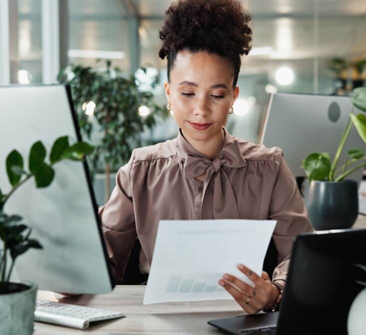 Business, woman and paperwork by computer in office for data entry in CRM system and reading revenue report. Account representative, employee and document for client sale stats and portfolio review.