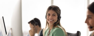 A smiling call center agent wearing a headset sits at her workstation, reflecting confidence, support, and advancement opportunities found in call center career paths.