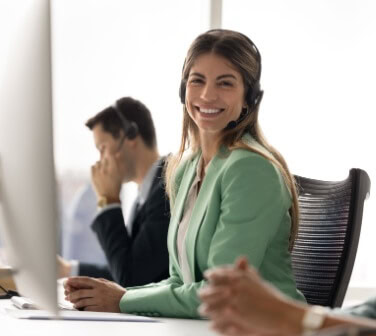 A smiling call center agent wearing a headset sits at her workstation, reflecting confidence, support, and advancement opportunities found in call center career paths.