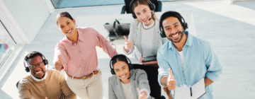 A diverse group of call center employees wearing headsets smile and give thumbs up, capturing confidence and teamwork during the call center first 90 days.