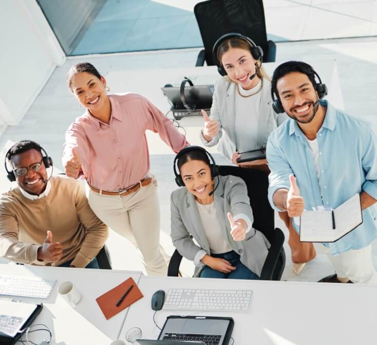 A diverse group of call center employees wearing headsets smile and give thumbs up, capturing confidence and teamwork during the call center first 90 days.