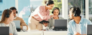 Supervisor guiding customer support agents with headsets in a bright office, showcasing collaboration and training in nearshore call center jobs.