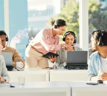 Supervisor guiding customer support agents with headsets in a bright office, showcasing collaboration and training in nearshore call center jobs.