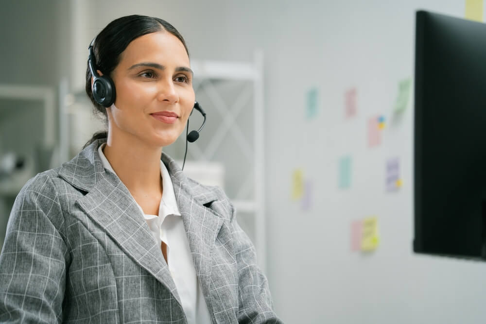 Professional customer service agent wearing a headset and assisting customers at her computer, representing nearshore call center jobs in a modern office environment.