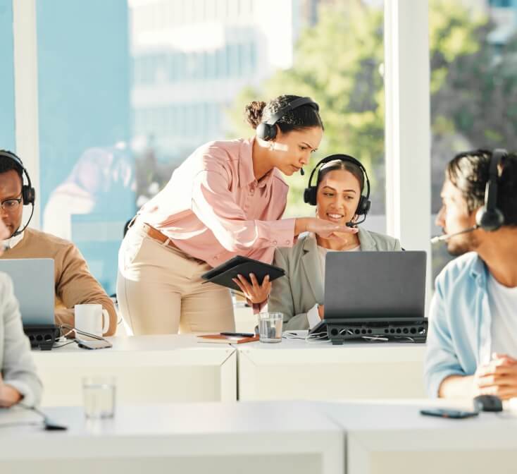 Supervisor guiding customer support agents with headsets in a bright office, showcasing collaboration and training in nearshore call center jobs.