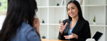 Recruiter in a black blazer speaks with a job candidate across a desk during an interview, reflecting call center recruiter expectations.