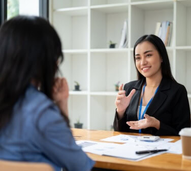 Recruiter in a black blazer speaks with a job candidate across a desk during an interview, reflecting call center recruiter expectations.