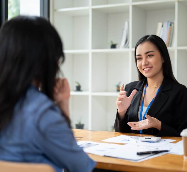 Recruiter in a black blazer speaks with a job candidate across a desk during an interview, reflecting call center recruiter expectations.