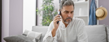 Man at home on the phone discussing an issue with a customer service call center, looking concerned on his couch-1