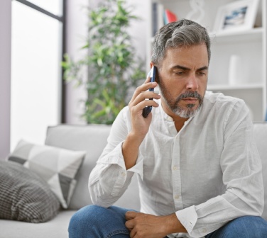 Man at home on the phone discussing an issue with a customer service call center, looking concerned on his couch-1