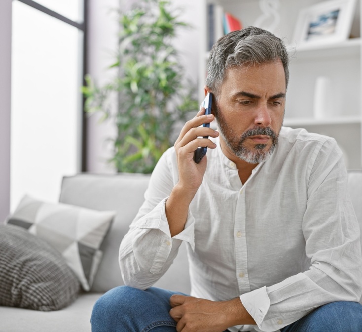 Man at home on the phone discussing an issue with a customer service call center, looking concerned on his couch-1