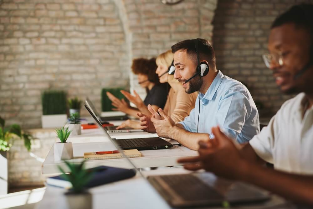 Call center agents wearing headsets collaborate at a shared desk with laptops and notes, showing why call centers are one of the most structured career environments for young professionals.