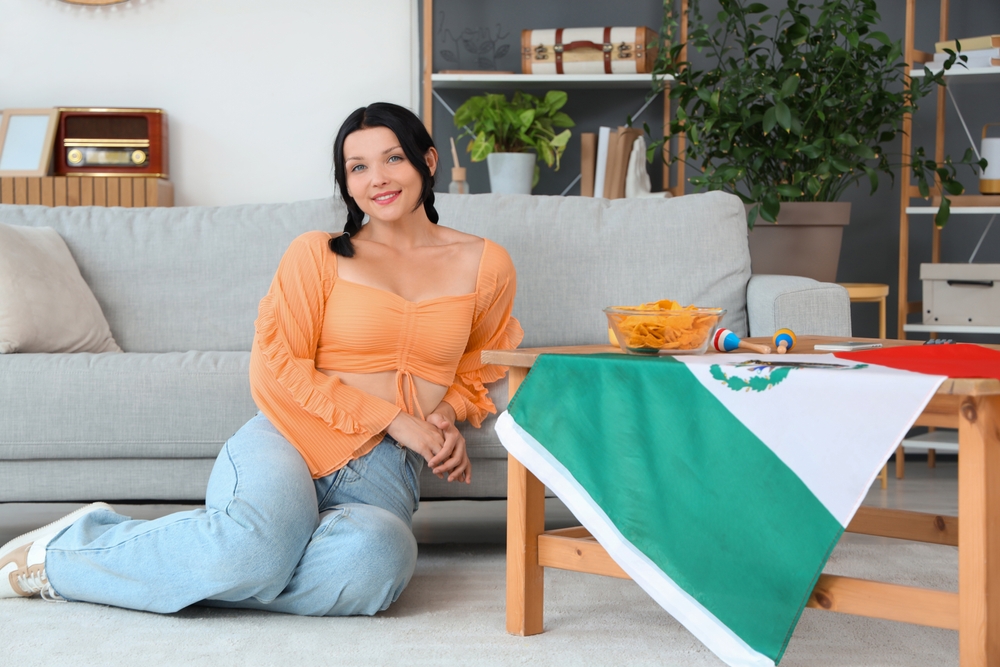 Young Mexican woman with flag at home she bought with her legal Mexico job benefits through Infonavit.