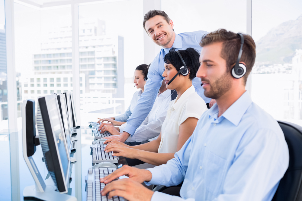 Side view of manager and executives with headsets using computers in a multicultural call center.

