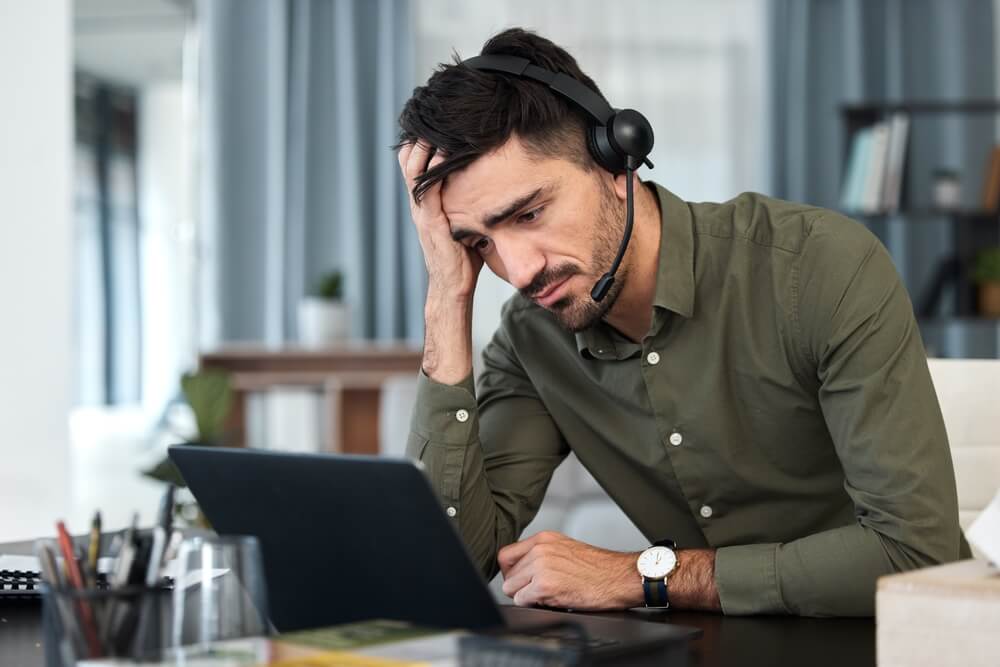 Stressed call center agent experiencing burnout while wearing a headset at their workstation, highlighting the importance of mental well-being, workload management, and employee support.