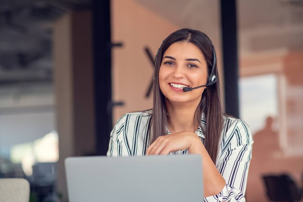 Smiling call center agent wearing a headset works from her laptop, showing how to build confidence when you’re new to taking calls.