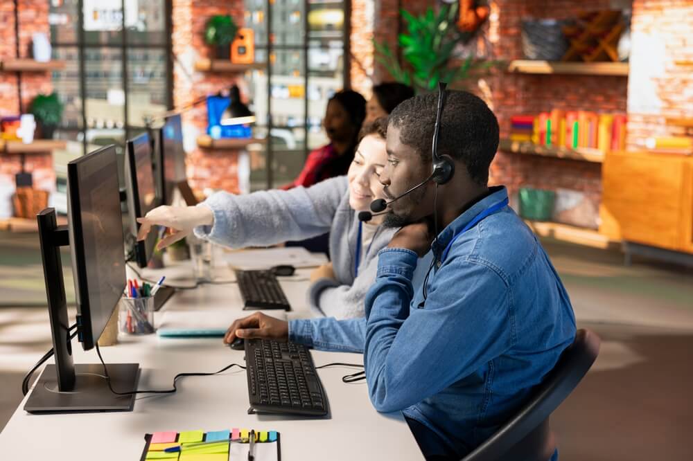 Trainer helps a new call center agent at his computer, showing how to build confidence when you’re new to taking calls.