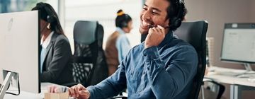 Smiling call center agent takes a customer call from his desk, showing how to build confidence when you’re new to taking calls.