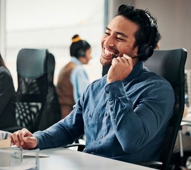 Smiling call center agent takes a customer call from his desk, showing how to build confidence when you’re new to taking calls.