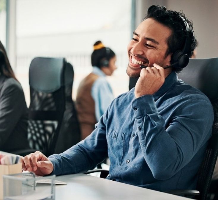 Smiling call center agent takes a customer call from his desk, showing how to build confidence when you’re new to taking calls.