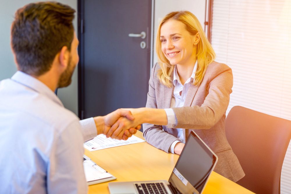 A job candidate shakes hands with a recruiter during an office interview while discussing how to find work in Mexico.