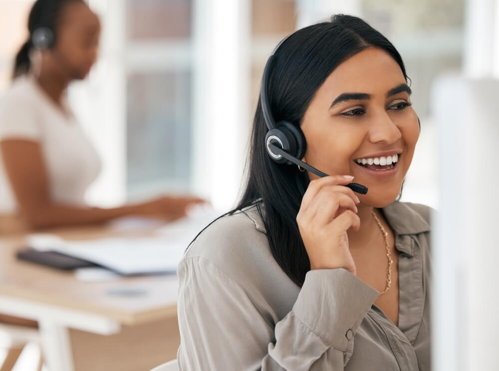Agente de call center sonríe mientras atiende una llamada con audífonos, reflejando confianza durante los primeros 30 días en un call center.