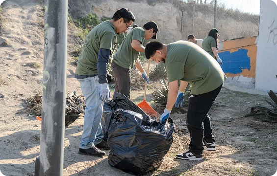 Un grupo de voluntarios recoge basura y la coloca en una bolsa grande al aire libre.