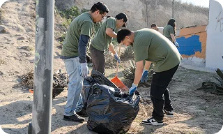 Un grupo de voluntarios recoge basura y la coloca en una bolsa grande al aire libre.