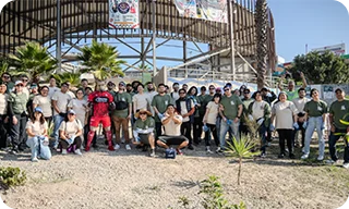 A large group of volunteers poses together outdoors in front of a structure after a community activity.