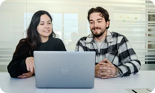 Two coworkers sit together looking at a laptop and discussing something on the screen.