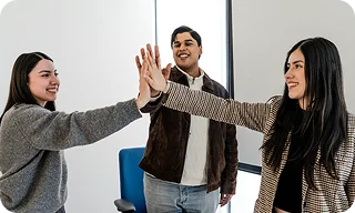 Three coworkers celebrate with a high five in an office setting.