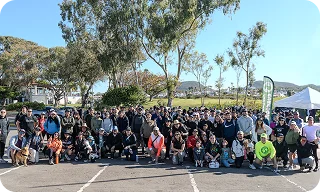 A large group of people gathers outdoors in a park setting, posing together during a community event.