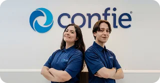 Two employees wearing Confie shirts stand back to back with arms crossed in front of a Confie logo wall.
