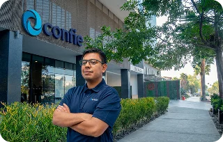 A man wearing a Confie polo stands with arms crossed outside a Confie office building.